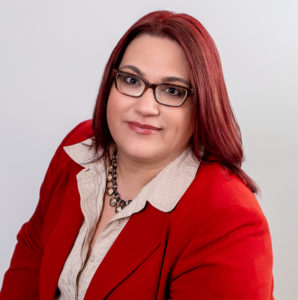A person with shoulder-length reddish hair and glasses, reminiscent of Elizabeth A. Calandrillo, Esq., is wearing a red blazer and white blouse. They are looking at the camera with a neutral expression against a plain white background.