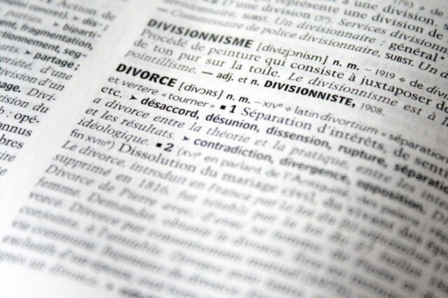 A close-up view of a dictionary page reveals the definitions for "divisionnisme" and "divorce" in French. The text is in black and white on textured paper, highlighting the difference between contested divorce and other entries with its clear print.