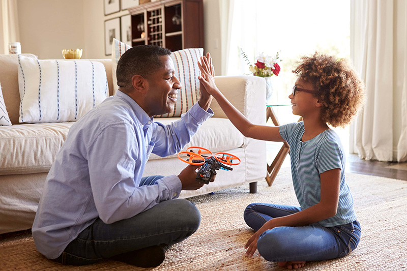 Side view of pre teen girl sitting cross legged on the floor of the sitting room giving a high five to her grandfather after building a model kit together close up