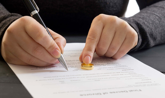 man signing divorce paperwork with ring on table