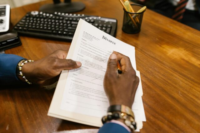 A person in a suit signs a Divorce Petition New Jersey at a wooden desk, with a keyboard, pen holder, and office supplies visible in the background.