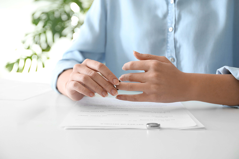 woman taking ring off with husbands ring sitting on documents